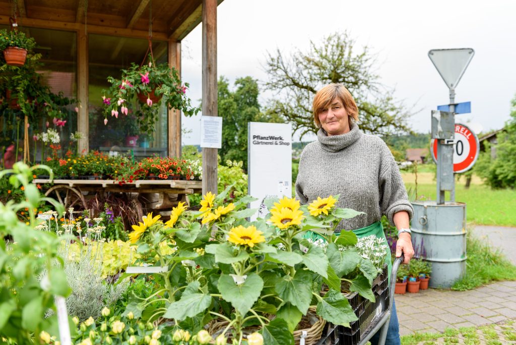 Mitarbeiterin mit Schubkarre voller Sonnenblumen vor dem 24h Shop des Gartenwerks